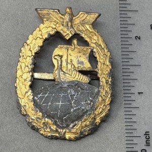 Vintage military badge with a ship and laurel wreath design, featuring gold and silver tones.