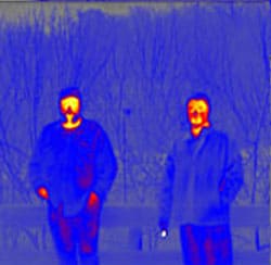 Two men standing outdoors in a cool blue, casual attire against a textured background.