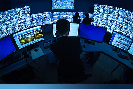 Multiple security monitors displaying surveillance footage in a high-tech control center.