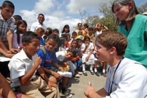 Children participating in a community outreach event with educators and volunteers outdoors on a sunny day.