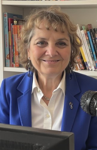 Professional woman in a blue blazer smiling in front of a bookshelf, representing media and communication expertise.