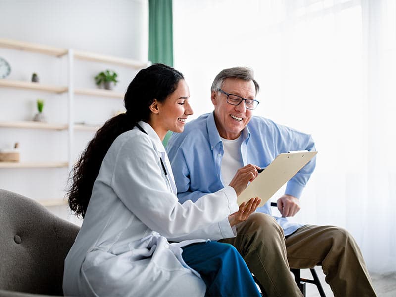 Young doctor asking senior impaired male patient in wheelchair to sign insurance policy at home