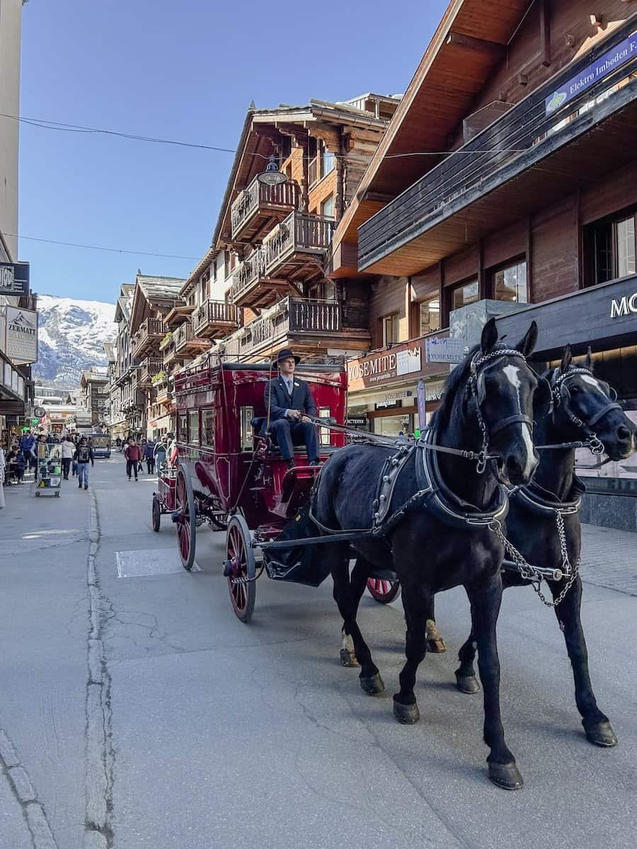 A horse drawn carriage is driving down the main street in Zermatt.