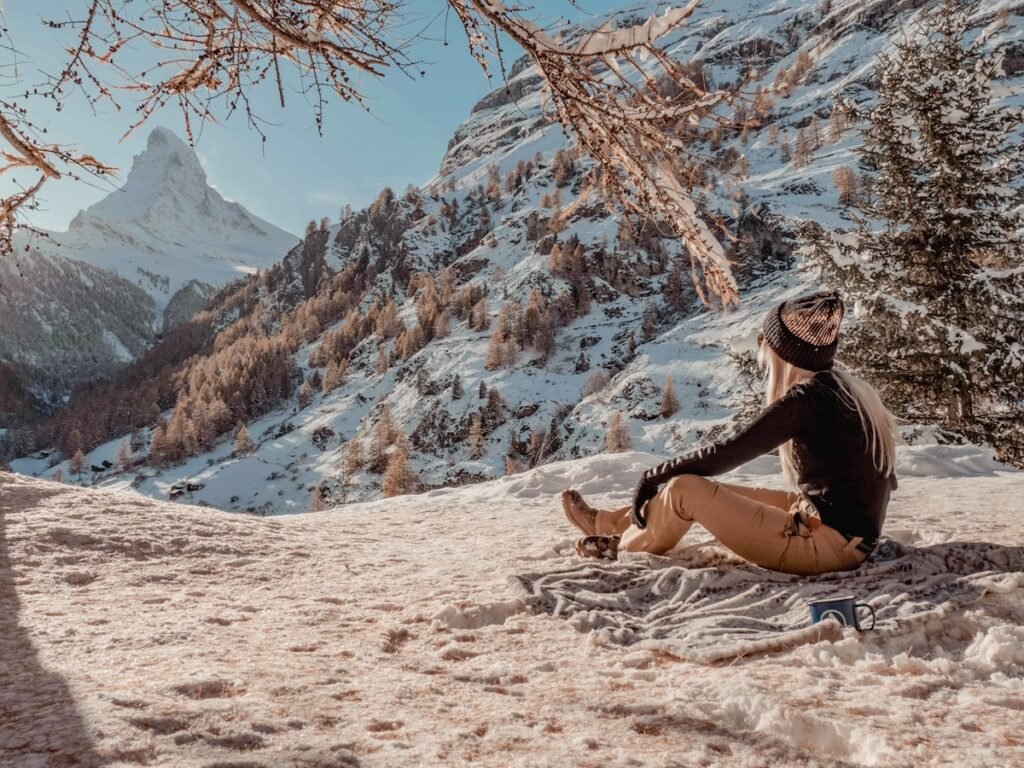 A woman sitting on a blanket on the snowy ground in front of the Matterhorn in late Autumn.