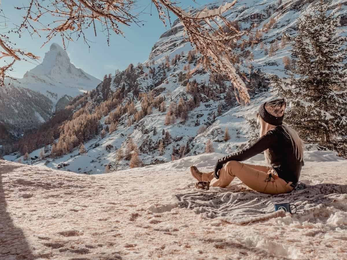A woman sitting on a blanket on the snowy ground in front of the Matterhorn in late Autumn.