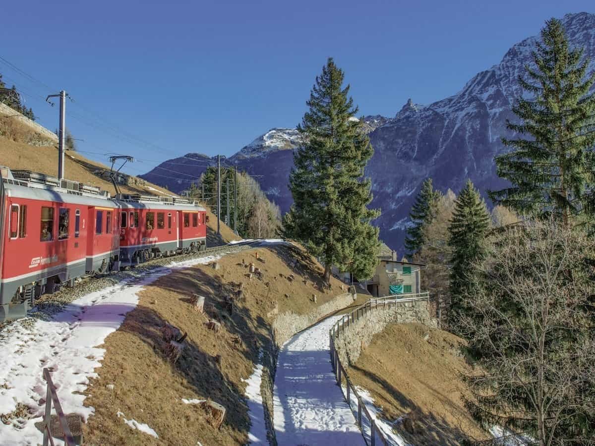 A red train travelling through the Swiss mountains.