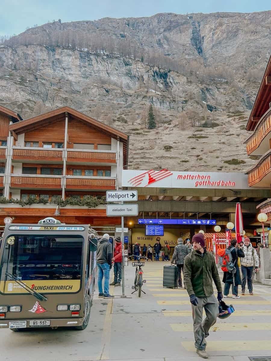 People and an electric taxi in front of Zermatt train station.