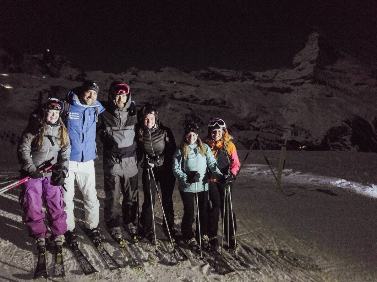 Skiers posing in front of the Matterhorn at night.