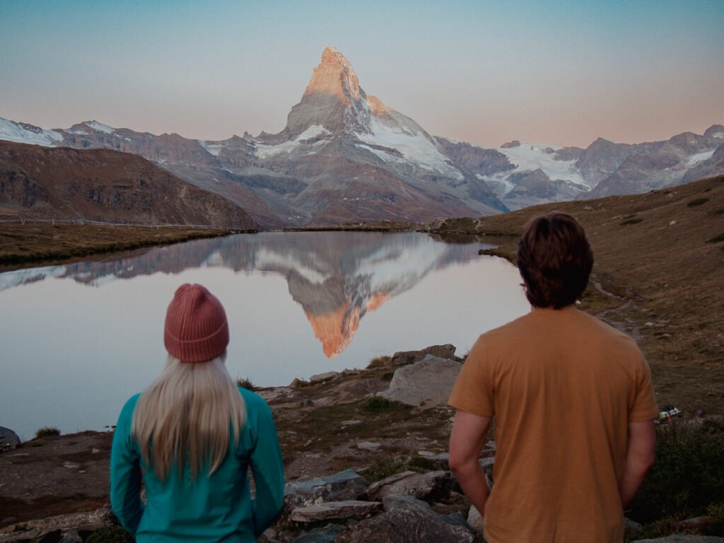 Couple watching the sunrise over the Matterhorn, with a lake reflection.
