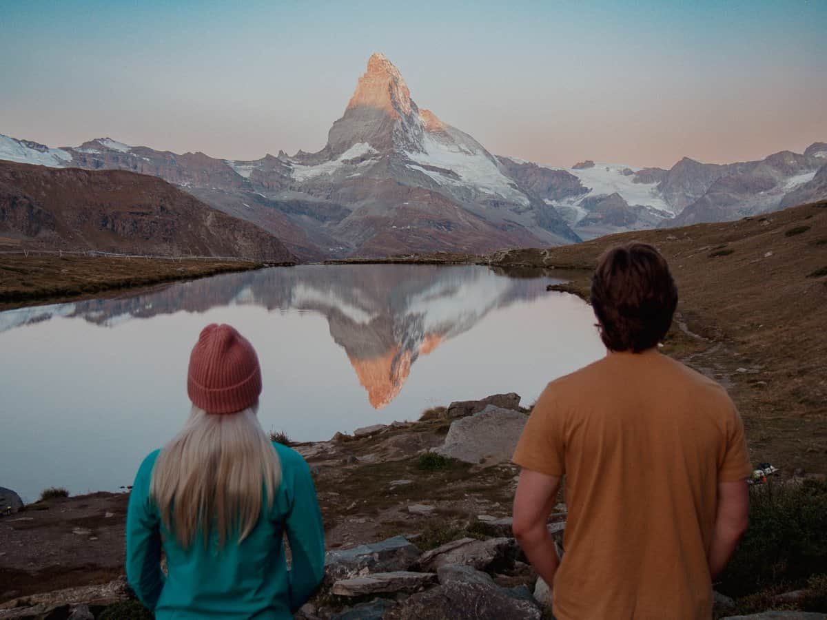 Couple watching the sunrise over the Matterhorn, with a lake reflection.