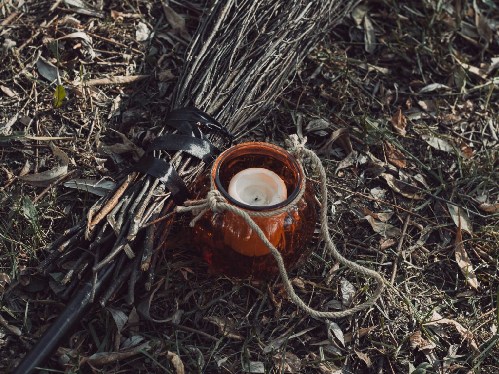 Broom and candle among leaves on the ground.