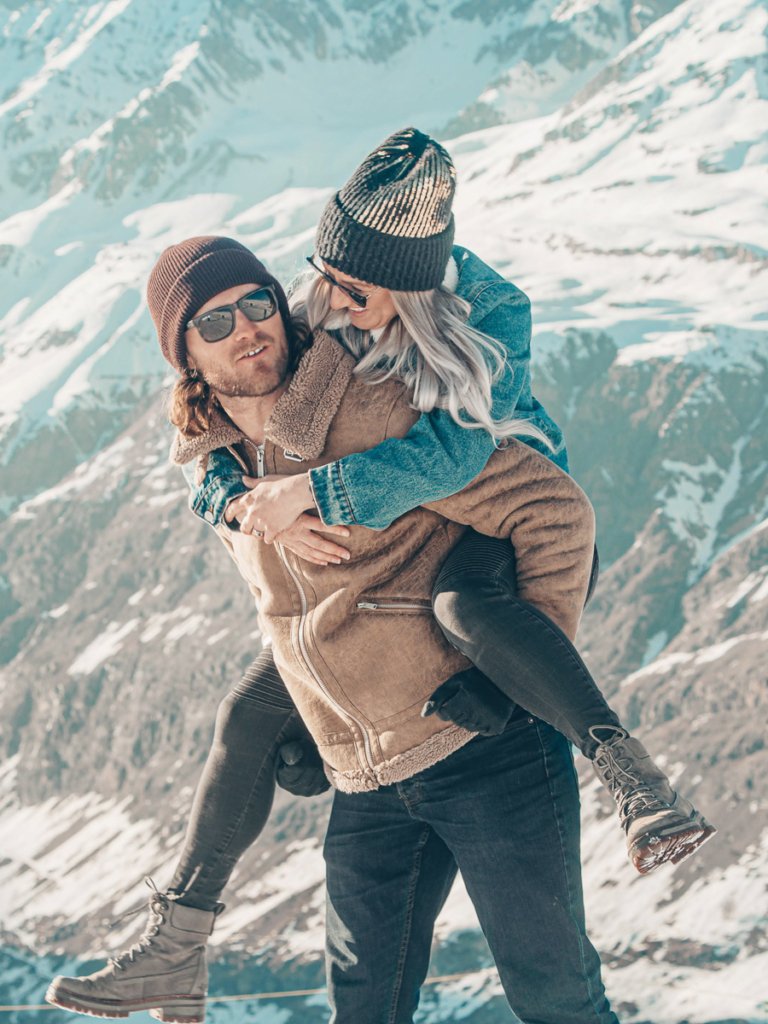 Man giving a woman a piggieback in the snow covered mountains of Zermatt.