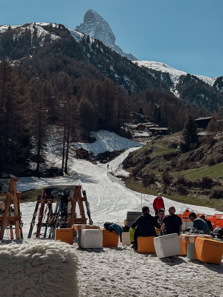 Skiers sat on cushions and deck chairs at Blatten, by the piste in Zermatt.