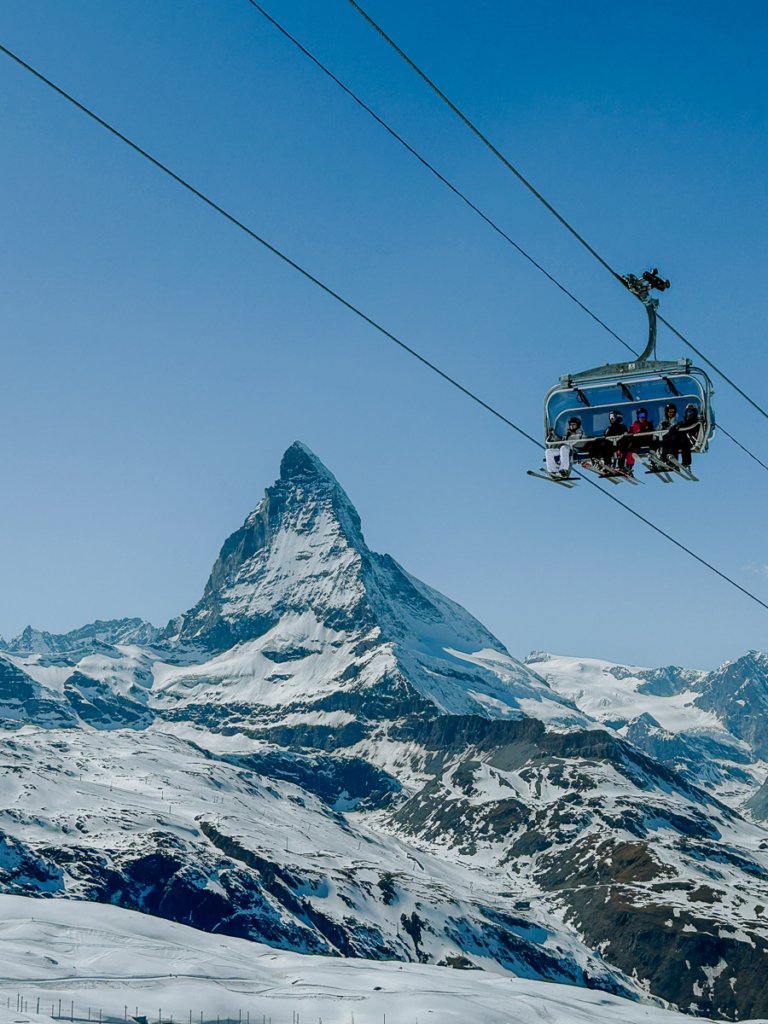 Skiers on a chair lift in front of the Matterhorn.