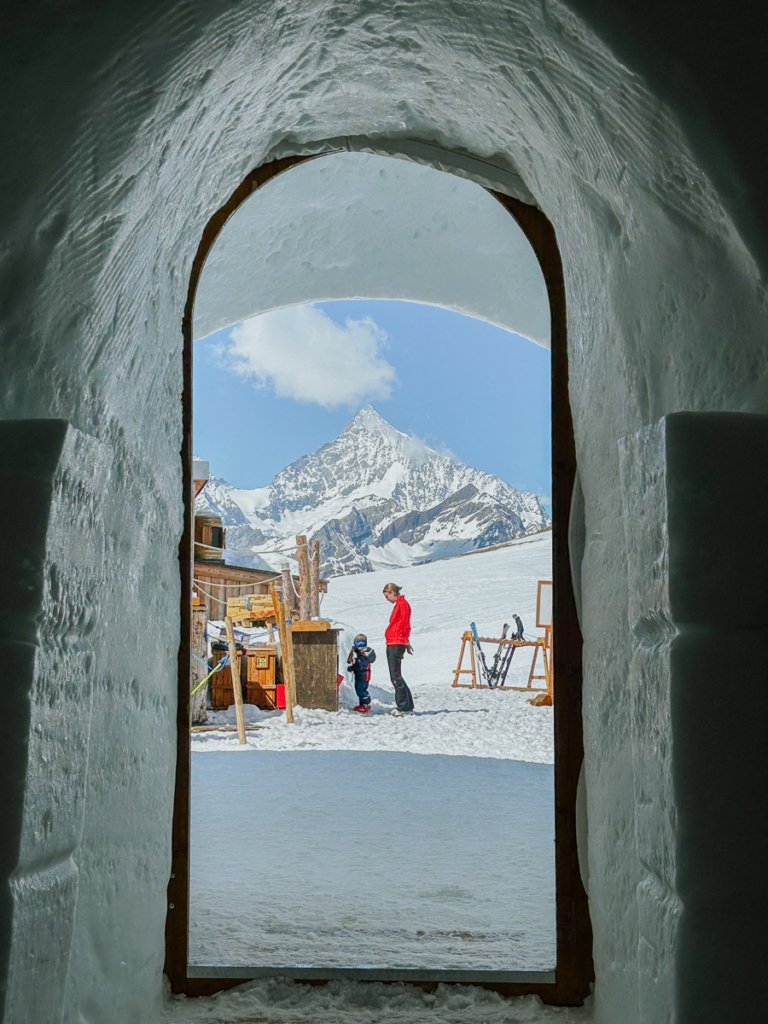 A view of skiing family and mountains through the doorway of an igloo in Zermatt, Switzerland.