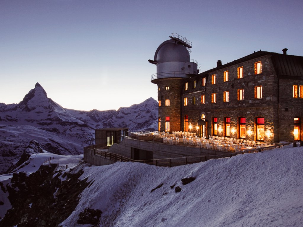 The Kulm Hotel and dining terrace lit up at night in front of the Matterhorn.