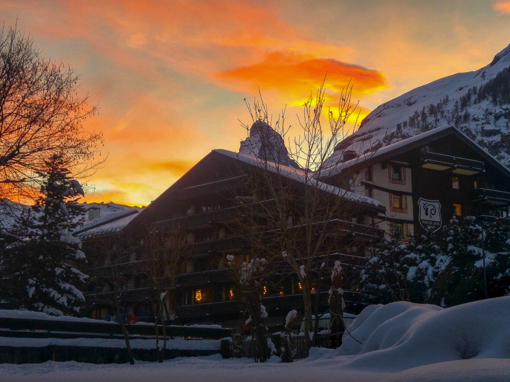 Fiery sunset above the Matterhorn and snow-covered Swiss chalets.