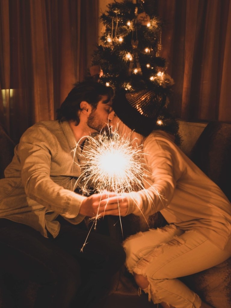 Couple kissing in front of a christmas tree holding a sparkler in Zermatt, Switzerland.