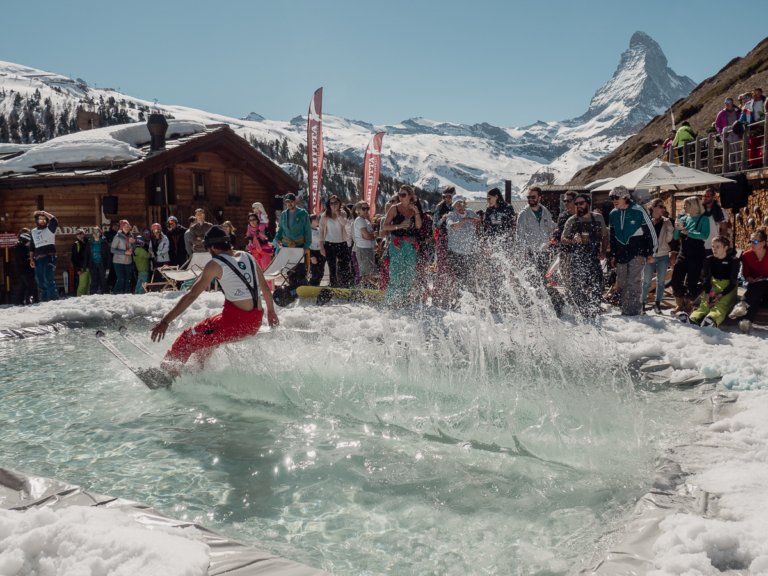 Skier sliding across a pool in front of the Matterhorn and a crowd.