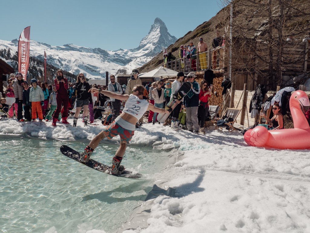Snowboarder sliding across a pool in front of the matterhorn and a crowd in Zermatt.