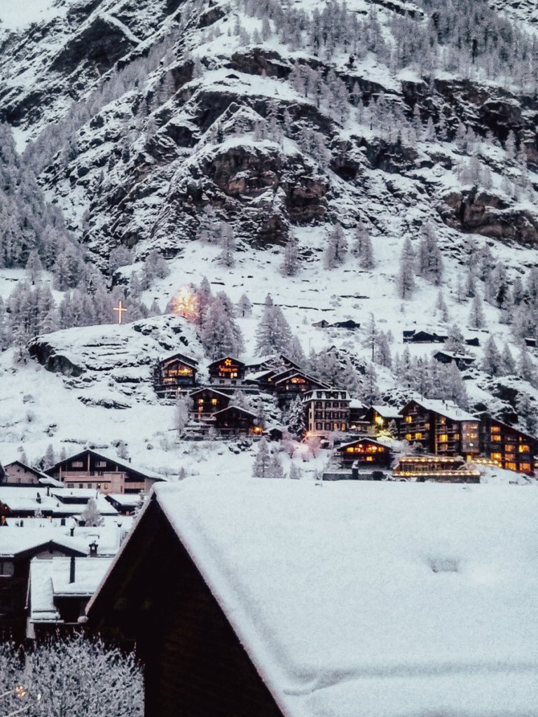 Snow covered buildings and lights at nighttime in Zermatt, Switzerland.