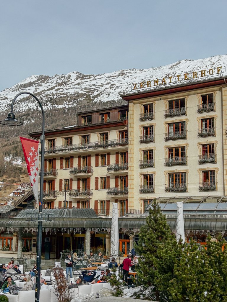 The Zermatterhof hotel and guests sat outside on a sunny spring day.