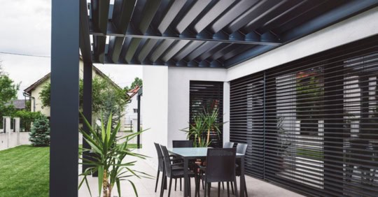Stylish covered outdoor dining space with black furniture and lush greenery.