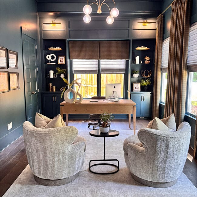 Stylish home office with navy blue walls, large windows, and modern decor.