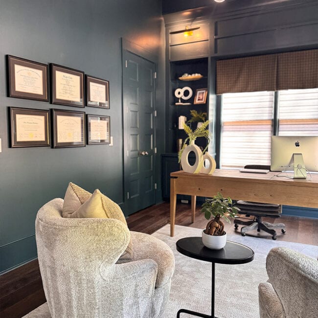 Cozy office space with armchairs, desk, and framed certificates on the wall.