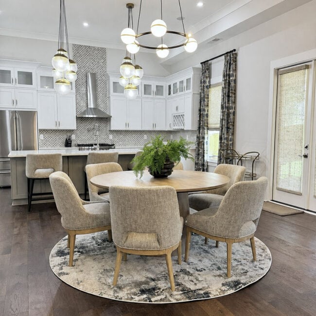 Bright kitchen with white cabinets and a round dining table with six chairs.