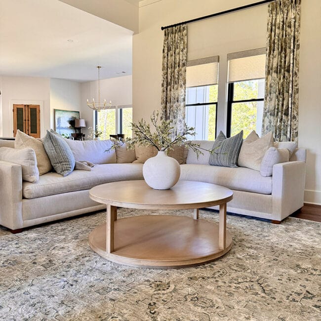 Bright living room with large windows, floral curtains, and cozy sofas.