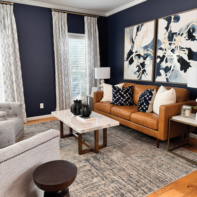 Modern living room with navy walls, brown leather sofa, and abstract art.