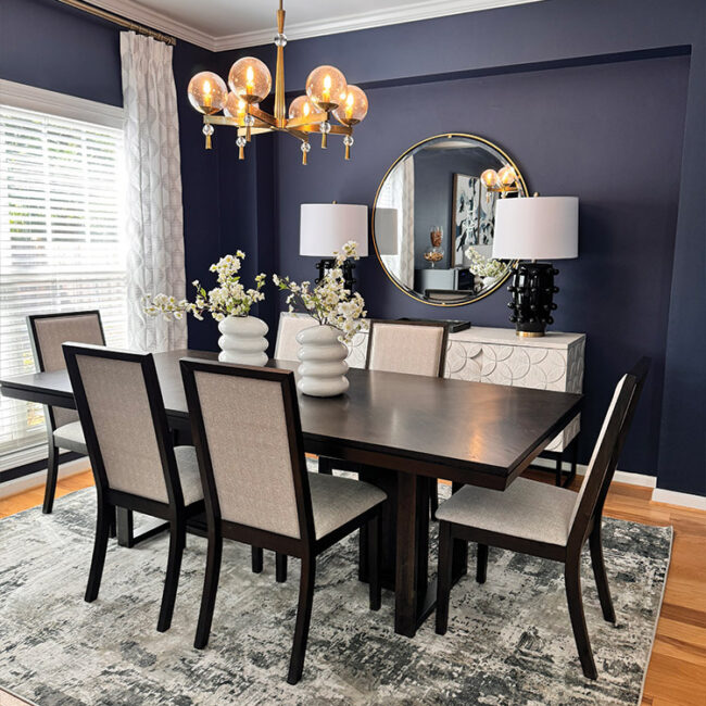 Elegant dining room with dark blue walls, six chairs, chandelier, and decorative mirror.