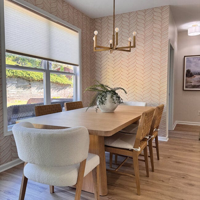 Bright dining room with large window, wooden table, and mixed chairs.