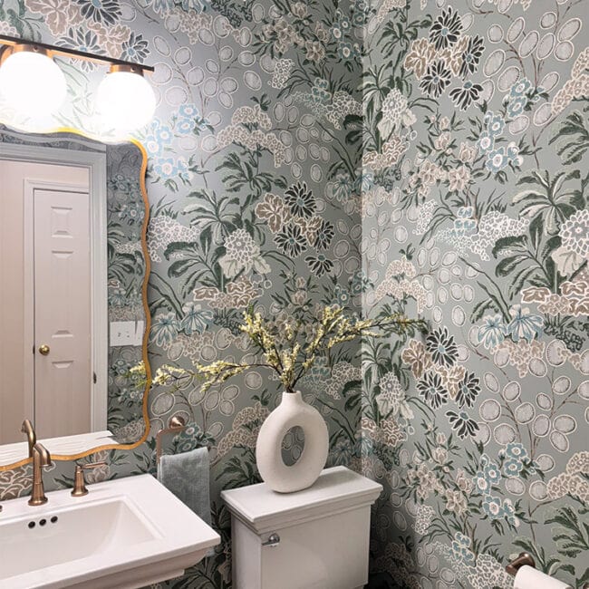Bathroom with floral wallpaper, white sink, mirror, and decorative vase.