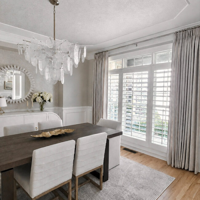 Bright dining room with large windows, white curtains, and modern chandelier.