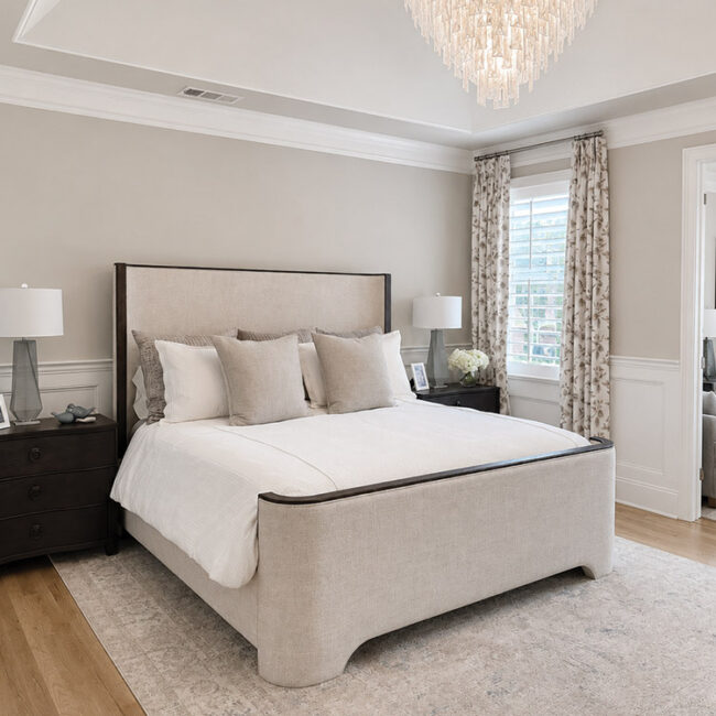 Modern bedroom with neutral tones, chandelier, and large window with curtains.