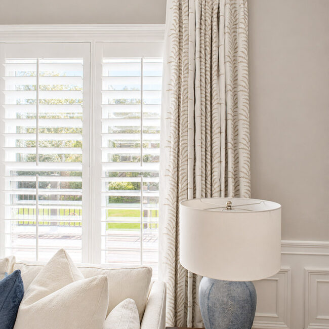 Living room with large windows, white curtains, and a beige sofa.