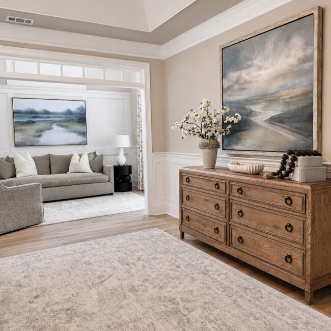 Stylish living room with large paintings, wooden sideboard, and floral decor.