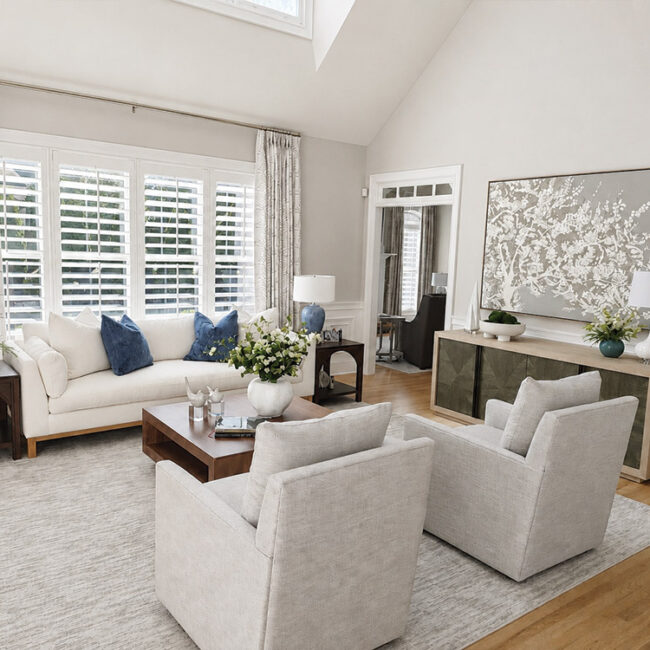 Bright living room with white sofa, armchairs, and large window with shutters.