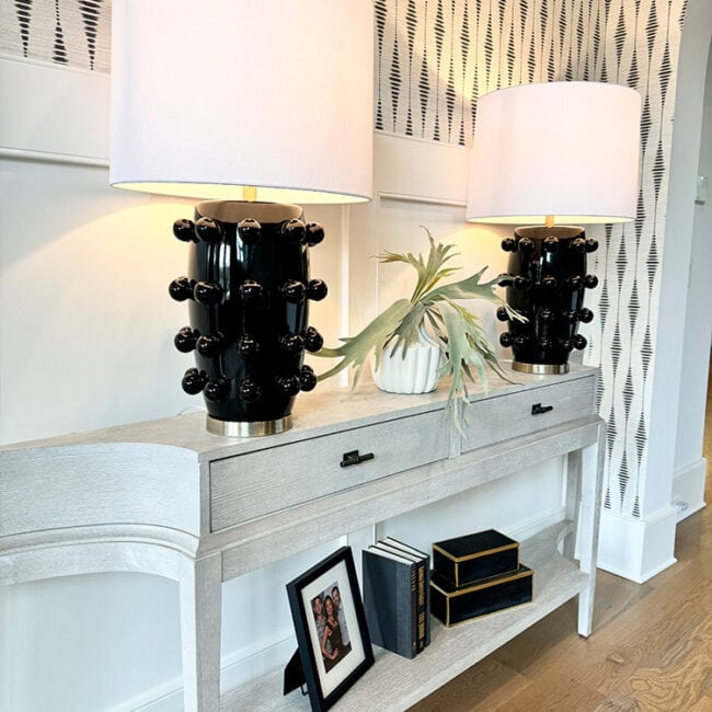 Two black and white table lamps on a white console table with decorative items.