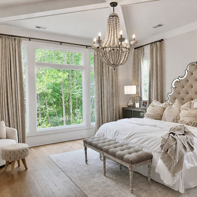 Bright bedroom with large windows, chandelier, and plush bed with tufted headboard.