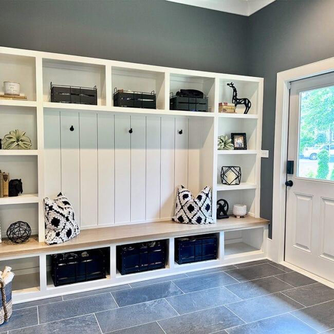 White built-in storage bench with black baskets and decorative pillows in entryway.