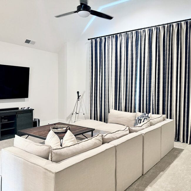 Spacious living room with a large flat-screen TV and striped curtains.