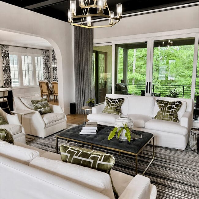 Bright living room with white sofas, black coffee table, and large glass doors showing greenery.