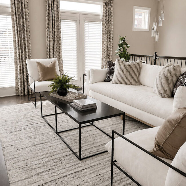 Bright living room with white sofas, black coffee table, and large windows with curtains.
