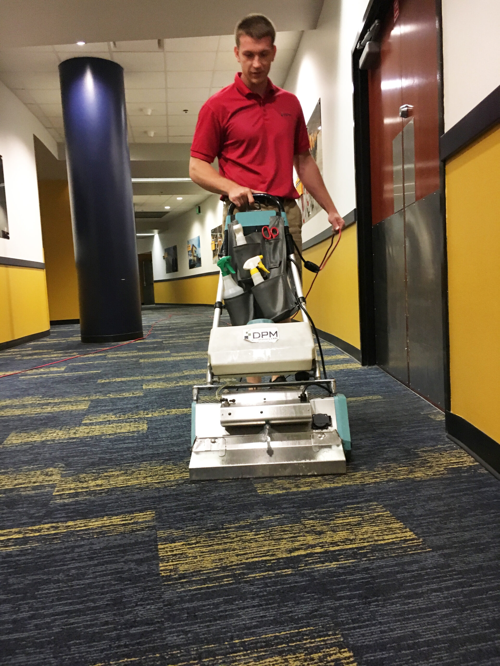 A man cleaning a carpet in a commercial office using a carpet cleaning machine. DPM Surface Care