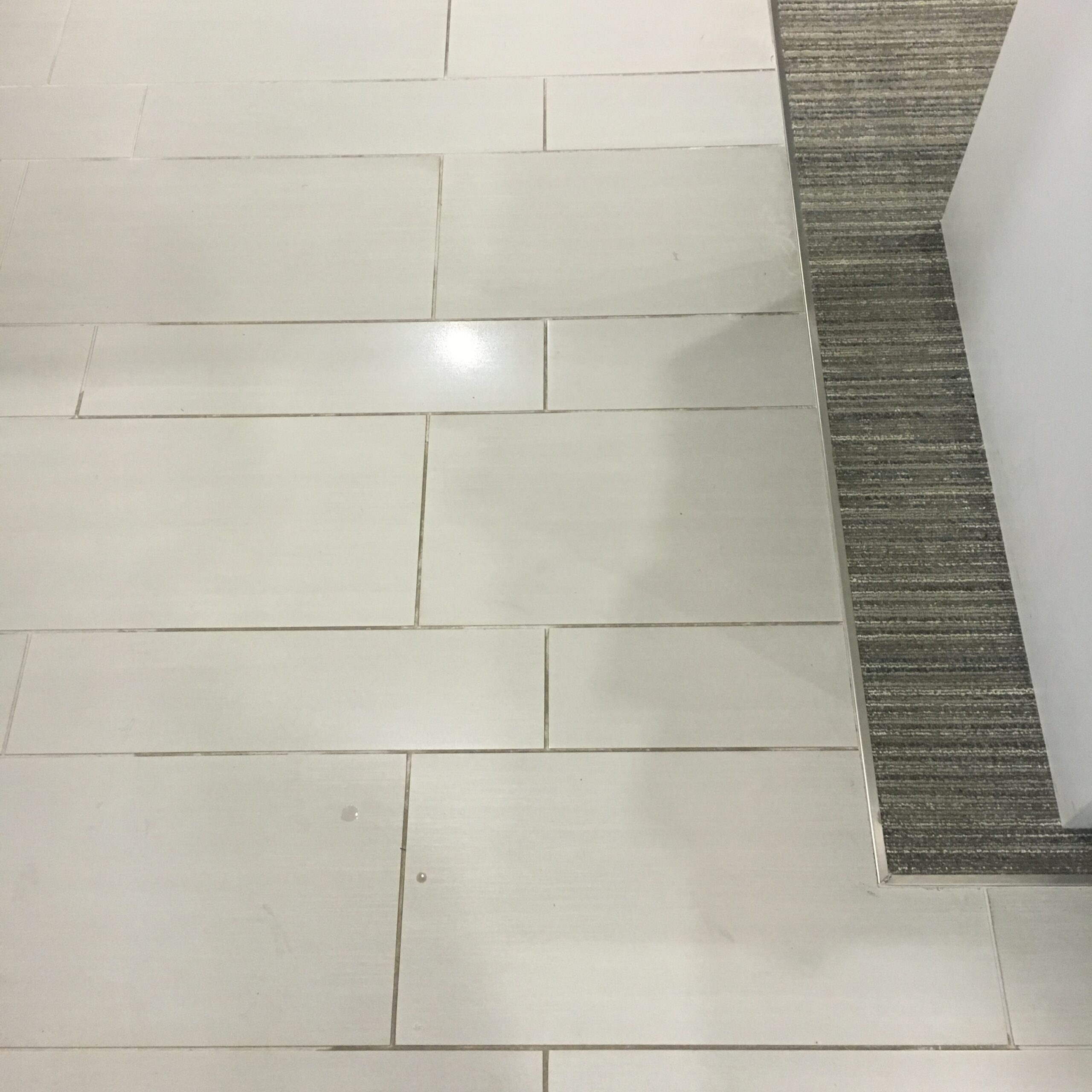 A white tile floor with dirty grout. DPM Surface Care