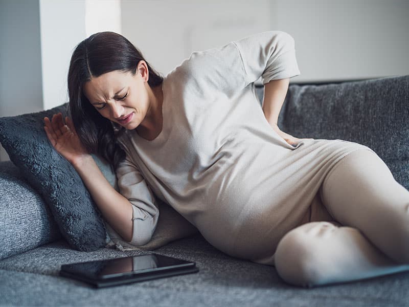 Severe lower back pain relief for pregnant woman lying on sofa.