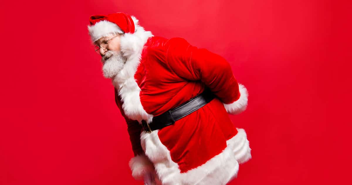 Santa Claus rubbing his back against a red background, wearing traditional red and white outfit.